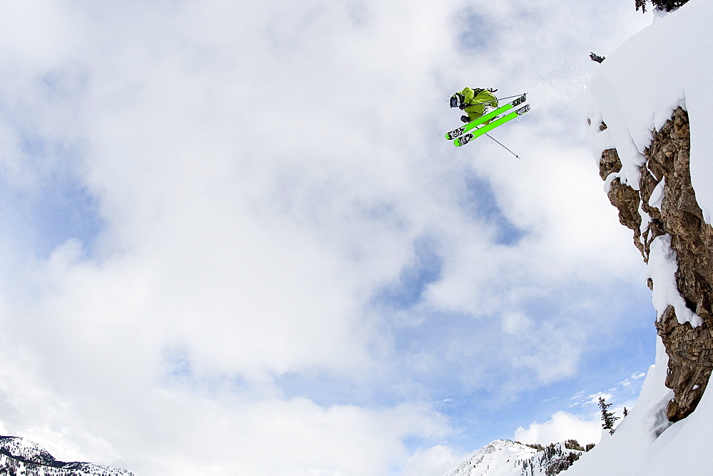 A male skier jumps off of a large cliff in the Wasatch backcountry, Utah.