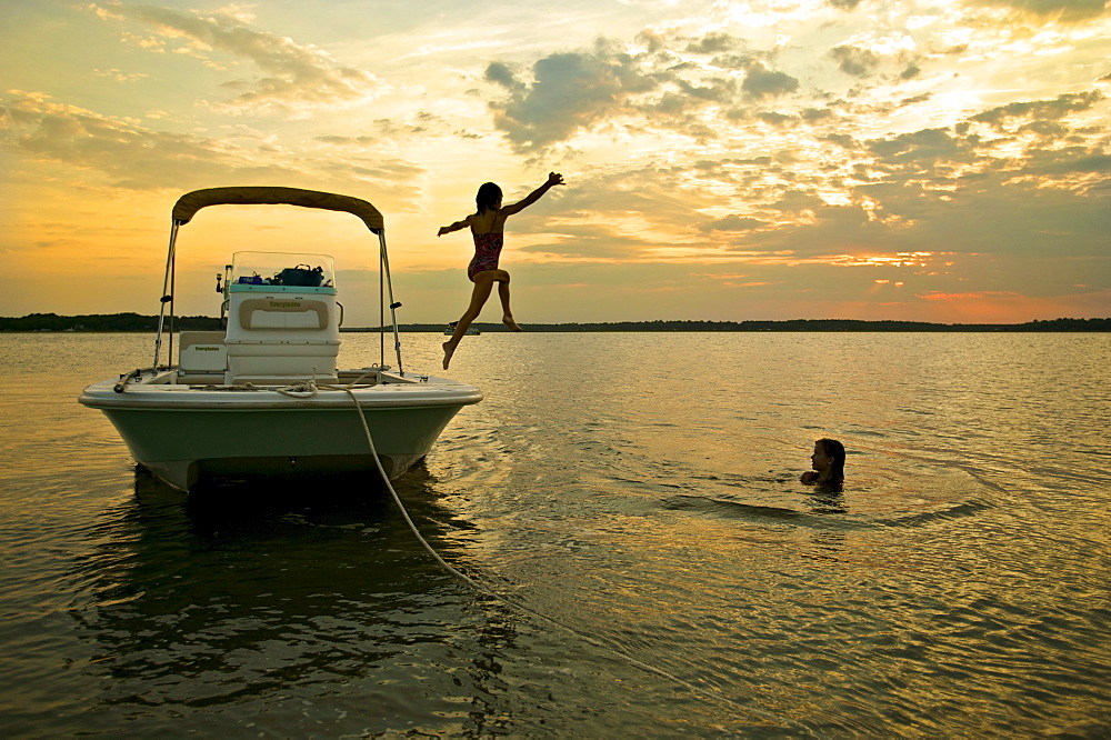 Children jumping off boat into water at sunset. McIntosh County, GA.