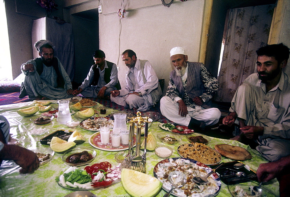 Afghan men and their guests eat a traditional feast of rice pilaf, mantu, and other dishes spread out on a plastic cloth, in an Afghan home in Mazar-i Sharif, Afghanistan