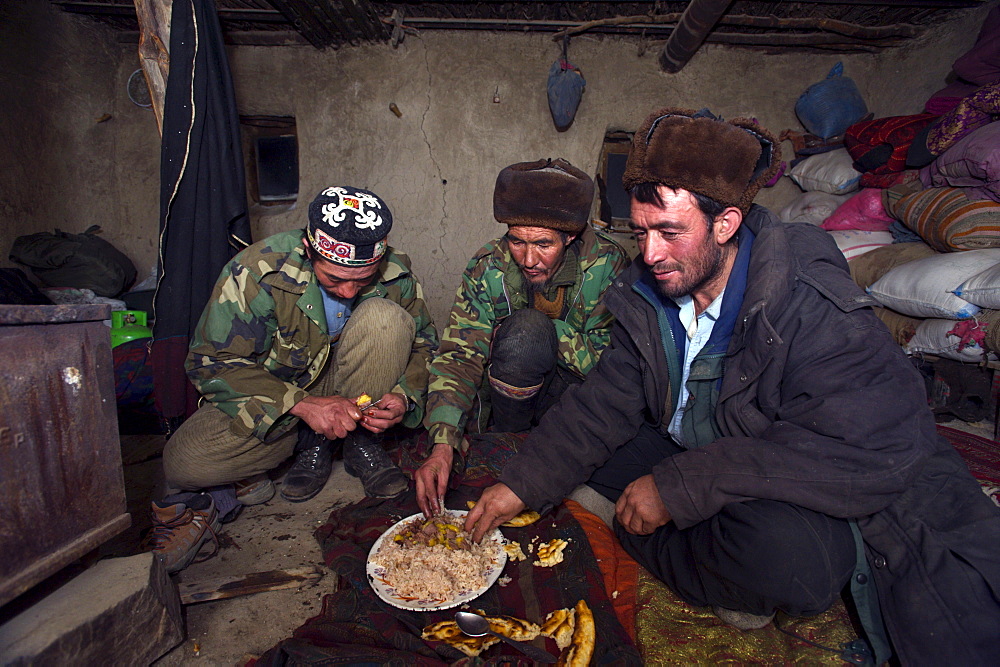 Kyrgyz and Wakhi men eat a simple meal of rice and bread in a mud hut at a winter camp in the Little Pamirs, Wakhan Corridor, Badakshan