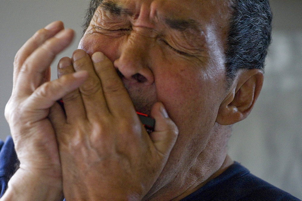 A man playing a harmonica in the morning in his home in Qaqortoq, Greenland