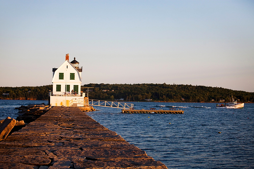 A lighthouse sits at the edge of a large, rocky dyke.