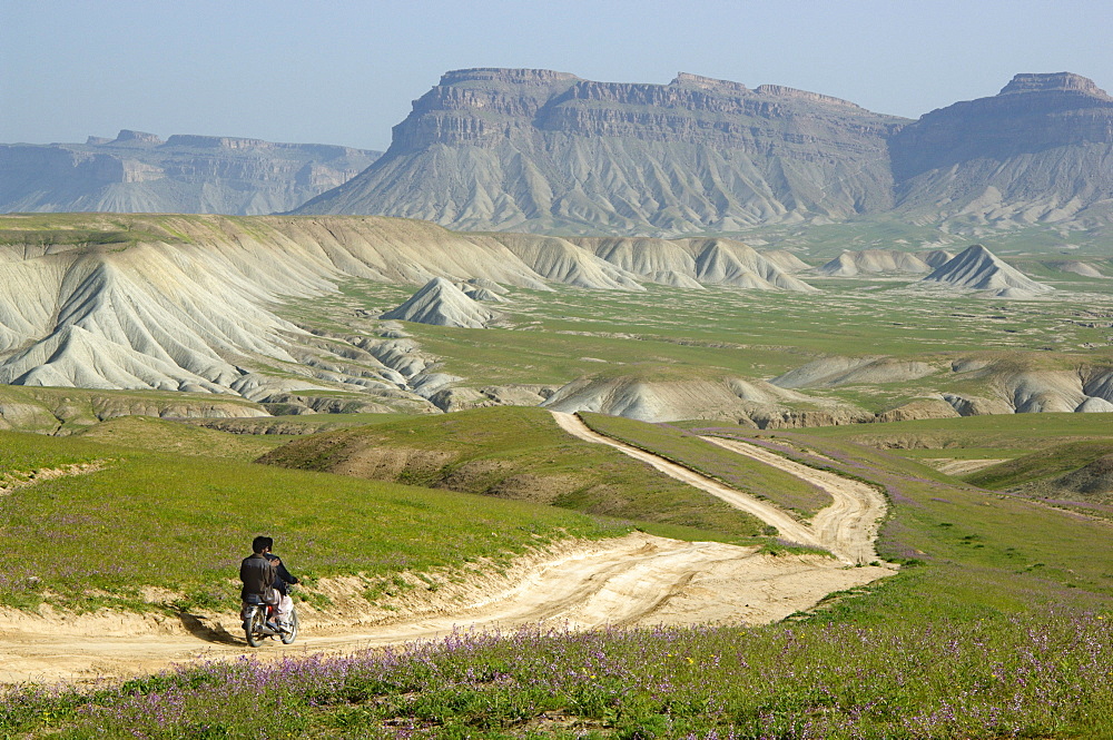 Young Baluch men on a motorbike ride on a dirt road through a desert landscape brushed with green after spring rains, in the Gulran district near the Iran and Turkmenistan border