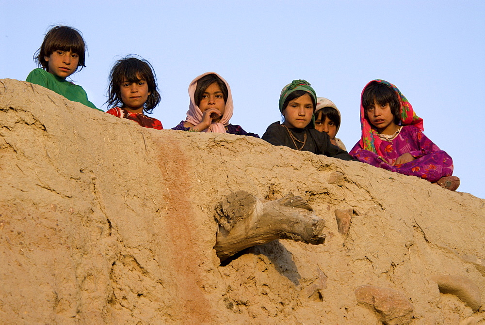 Young girls peer over the wall of a mud home in the Tajik village of Dera Jawal, at the base of the Band-e Baba range,  Herat Province, Afghanistan