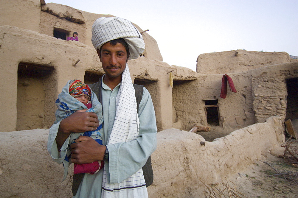 Young Tajik man holds his newborn son, in the    compound of his home, in the Tajik village of Dera Jawal, at the base of the Band-e Baba range,  Herat Province, Afghanistan