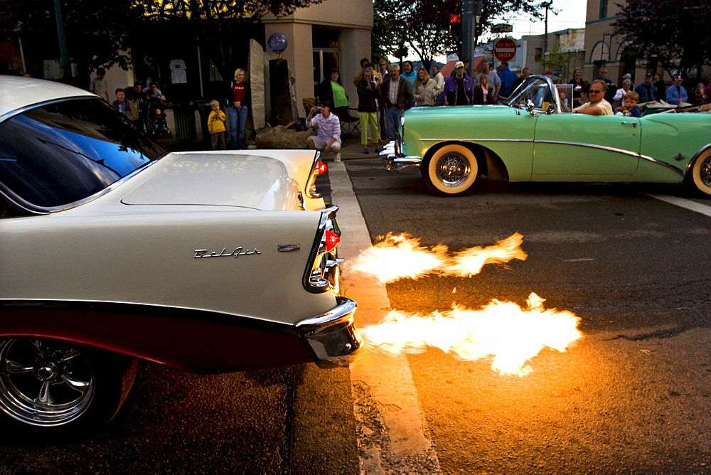 Spectators stand along a street watching a vintage car with a flaming exhaust in Coeur d'Alene, Idaho.