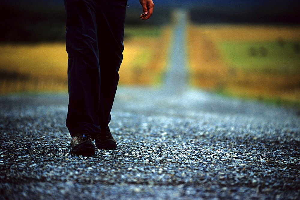 A lone, young man walks along a long, empty, prairie, dirt road found along the foothills that border the Rocky mountains in southern Alberta during October of 2005. Much of this area of low population density, large ranches and farms nestled at the base of the southern Rocky mountains is changing hands to concentrations of people in tight and clustered housing with paved roads.