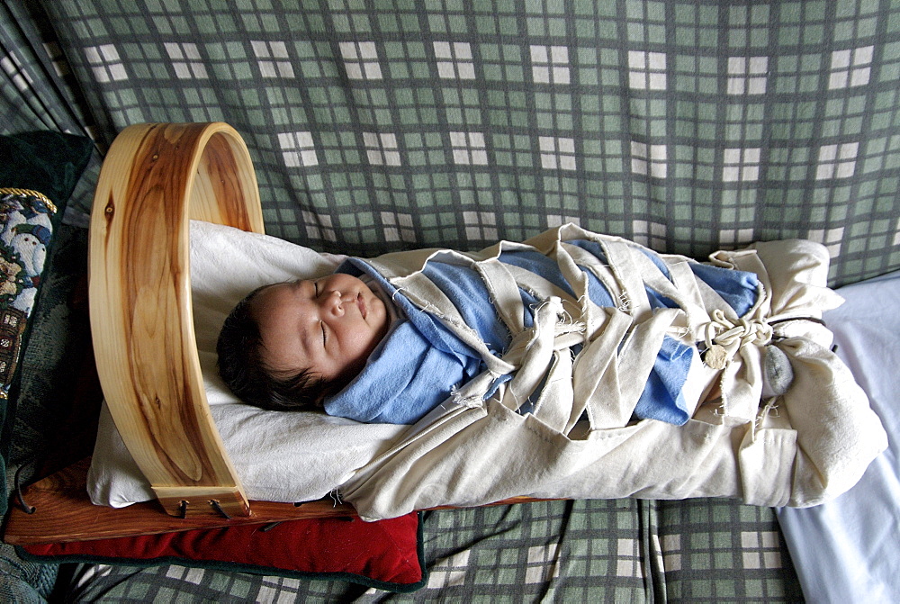 Stephan Begay, five week old Native American Indian baby naps swaddled on a backboard at home on the Navajo Reservation in Northeastern Arizona on March 22, 2007. The baby's mother is Hopi and the father is Navajo, so the baby is part of two tribes. There is a small Hopi Reservation in Kykotsmovi Arizona that is located within the very large Navajo reservation in the northeastern corner of the state, yet intermarriage is rare. Babies are kept on traditional  backboards until they start to crawl.