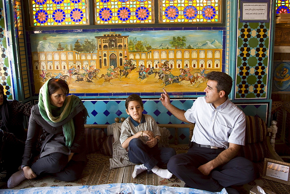 Esfahan, Iran - February, 2008: Iranian family having lunch in a colorful traditional looking restaurant on Imam Square in Esfahan, Iran.