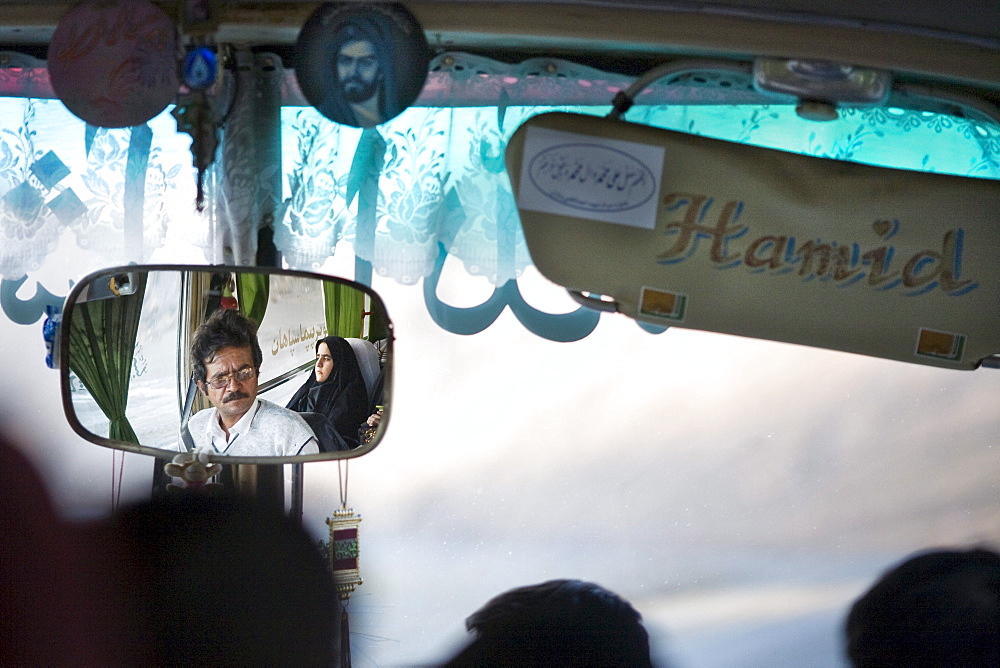 Dasht e Kavir, Iran - February, 2008: Bus driver and female passenger dressed in black reflected in the mirror of a bus enroute through the desert from Esfahan to Khur in Central Iran.