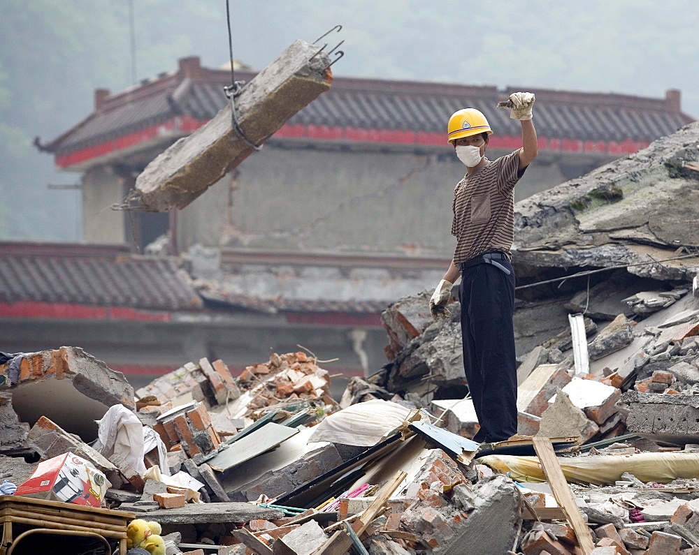 A rescue worker directs a crane where to move a large chunk of concrete from a building that collapsed during a powerful earthquake in Hongbai Vilage, China.