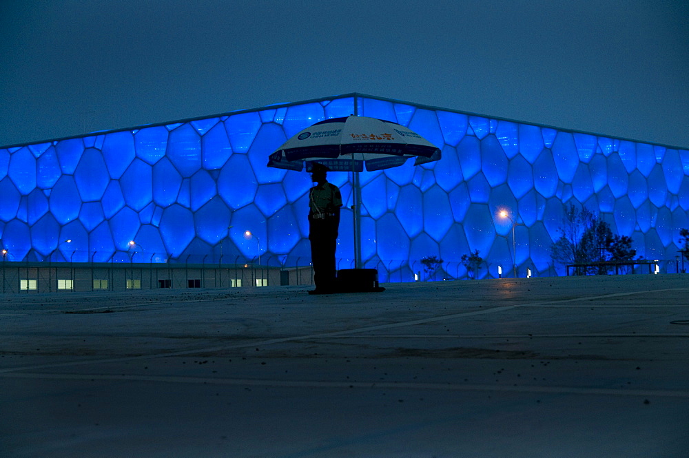 CHINA/Beijing/National Aquatic Center/17June2008:A soldier stands guard outside the National Aquatic Center at night. Designed by Australia's PTW Architects, its facade appearing as a cube of soap bubbles, it seats 17,000 people. The exterior is made from a high-tech lightweight translucent plastic that is also very energy efficient in saving an estimated 30% in power consumption by comparison to a traditional design. It houses 5 pools - one able to create it's own waves. It's outer surface looks like soap bubbles. It will host all swimming and diving events at the 2008 Olympics.