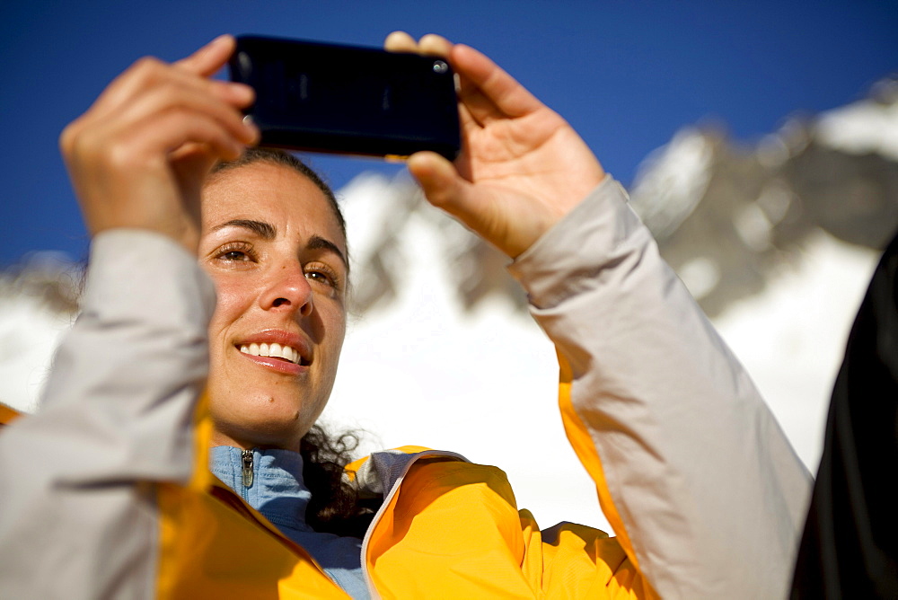 A Latina woman takes a cell phone picture in the mountains.