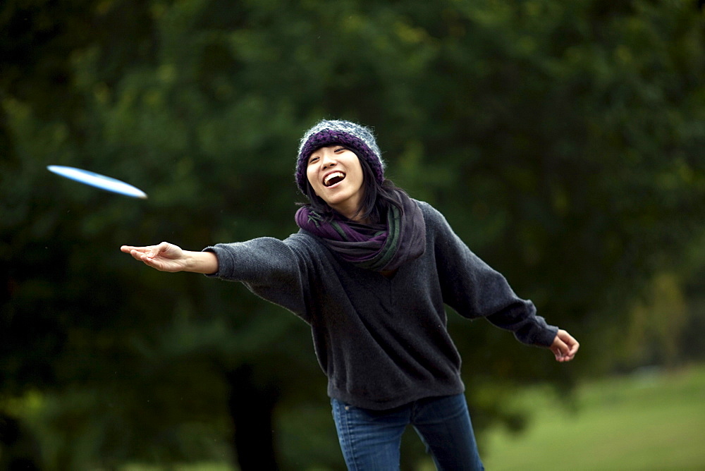 A young Asian-American woman throws a flying disk while playing flying disk golf in Baltimore, Maryland.