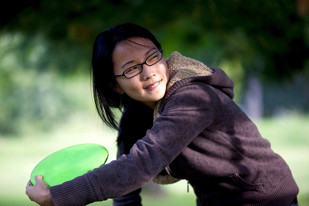 A young Asian-American woman plays flying disk golf in Baltimore, Maryland.