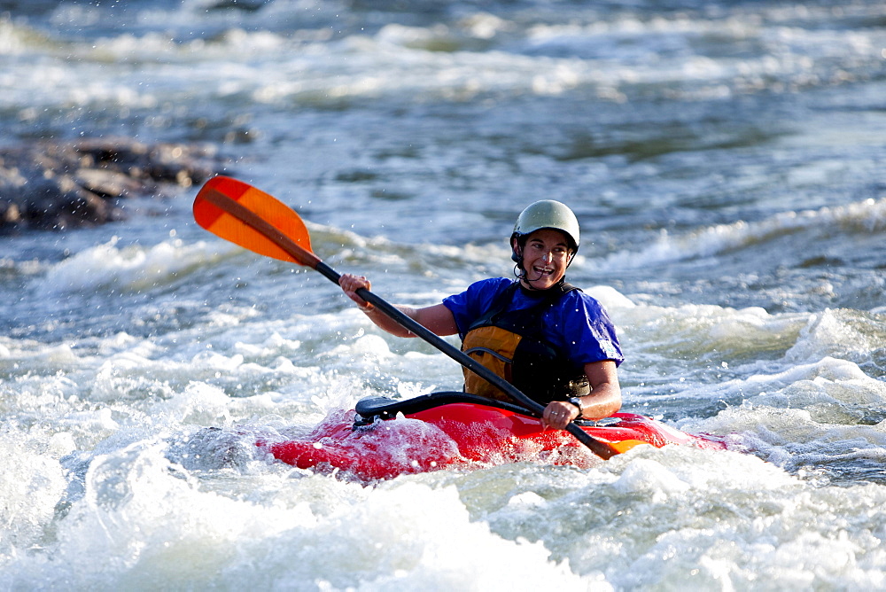 A female kayaker in a playboat paddles through rapids on the Clark Fork River, Missoula, Montana.