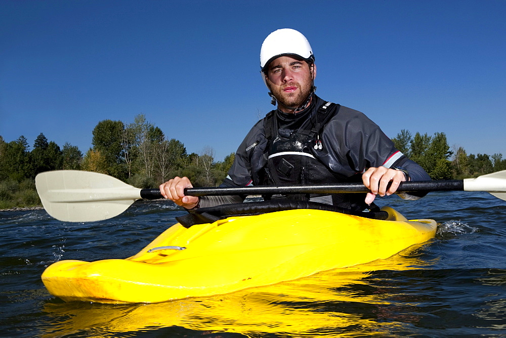 A male kayaker in a yellow playboat looks into the camera on the Clark Fork River, Missoula, Montana.