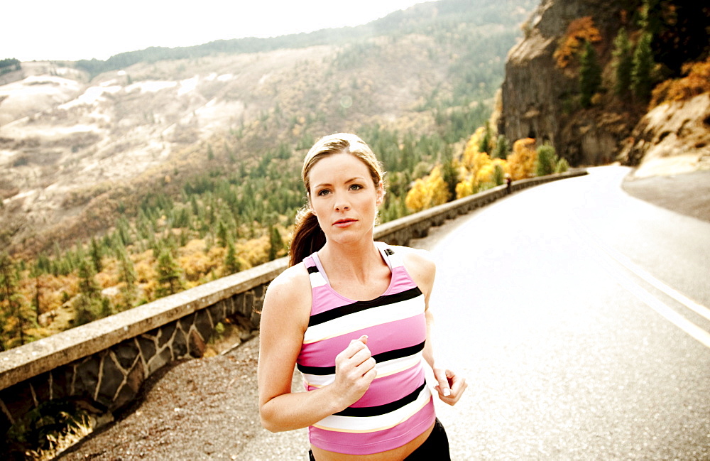 An athletic woman jogging along a deserted road on a beautiful fall day.
