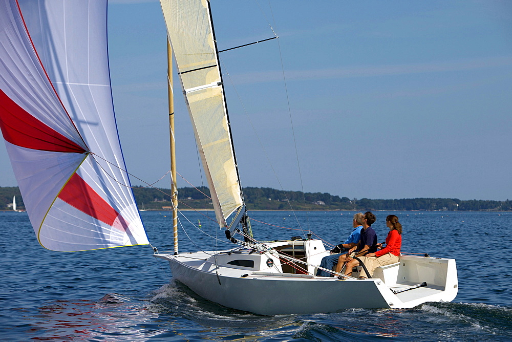 Three adults enjoying a sunny day on board a daysailer on Casco Bay, Maine.