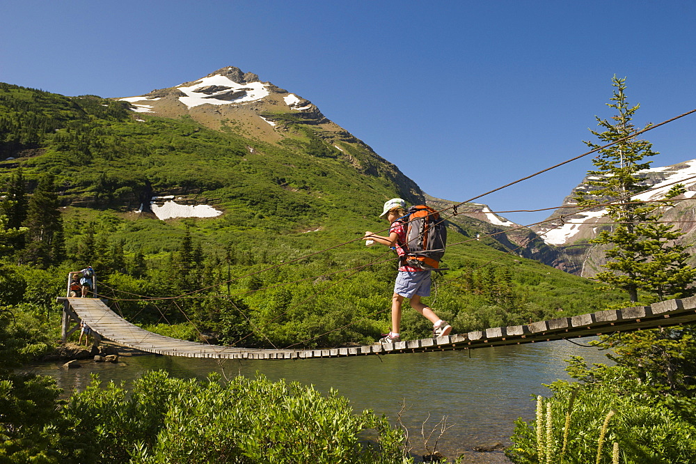 A young girl hikes over a suspension bridge in Glacier National Park, Montana.