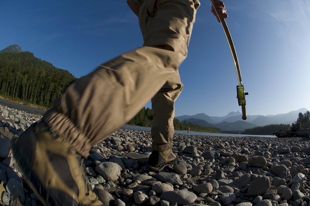 A man holding a fishing rod walks to the river to go fly fishing in Squamish, Brithish Columbia. (motion blur)