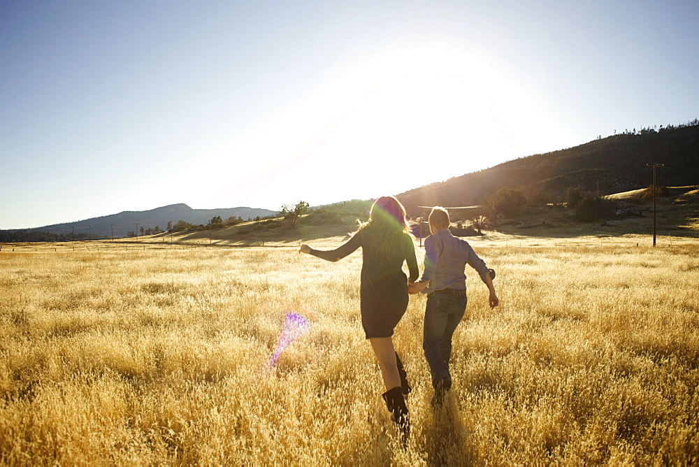 Couple hold hands and run together in an open field.