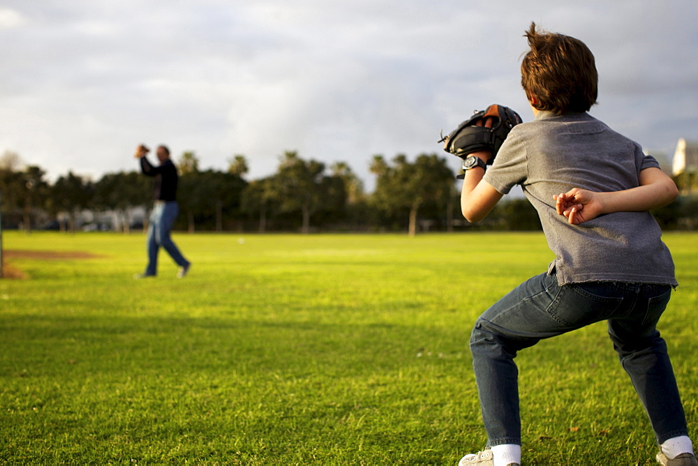 A kid wearing a baseball glove waits for his dad to throw the ball at the park.