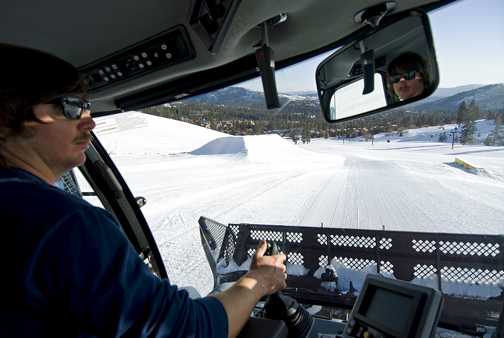 A young man prepares the ski hill for the day by grooming each run in Truckee, California.