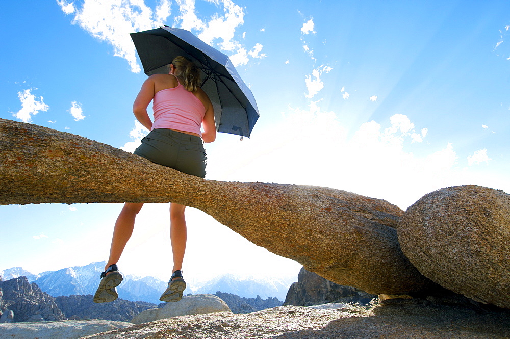 A woman sitting on a natural rock arch holding an umbrella.