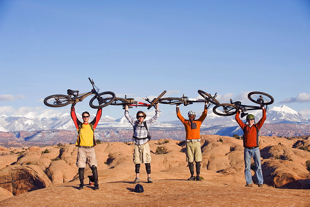 Four young men hold their bikes above their heads on the Slickrock Trail, Moab, UT.