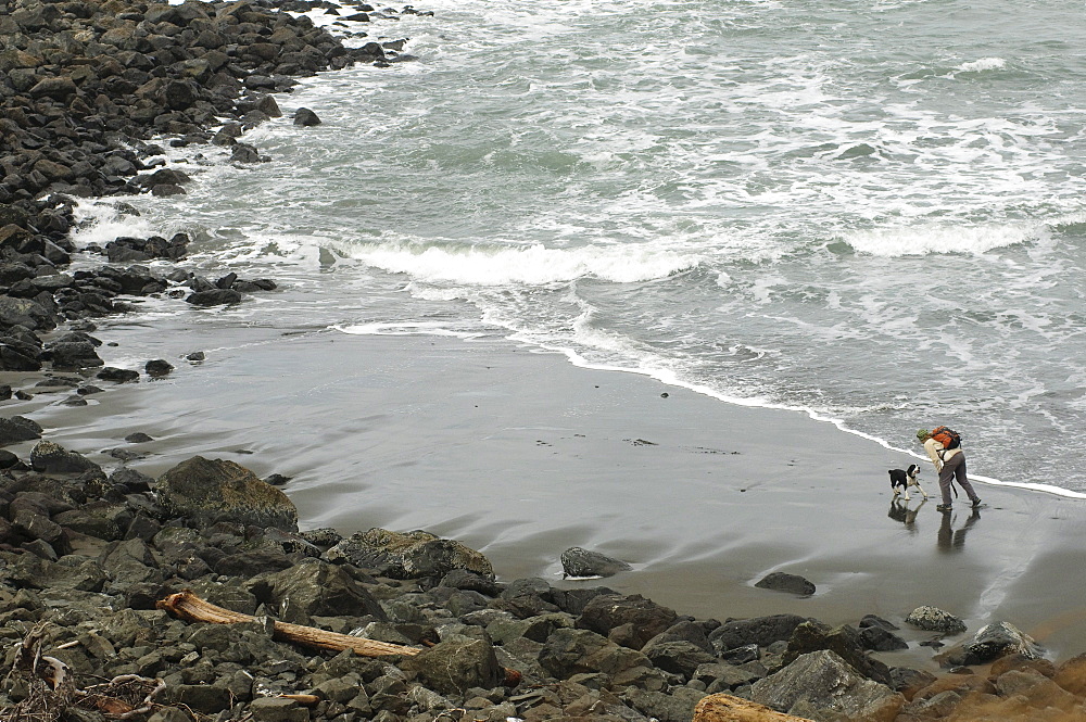 A woman hikes on a beach with her dog on the Oregon Coast.