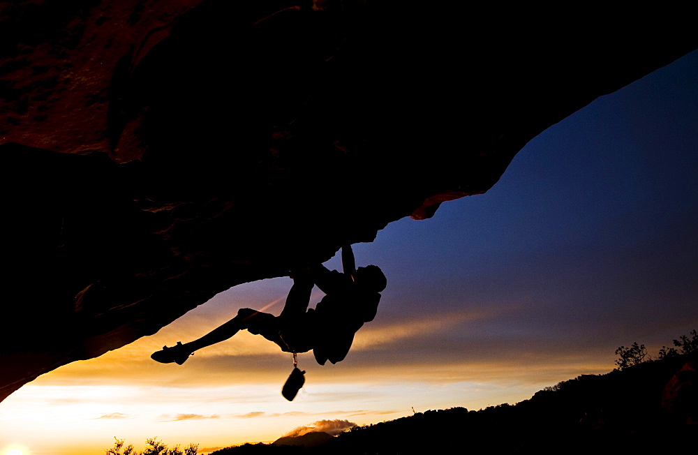 A young man climbs a boulder problem during a sunset overlooking the ocean in Santa Barbara, CA.
