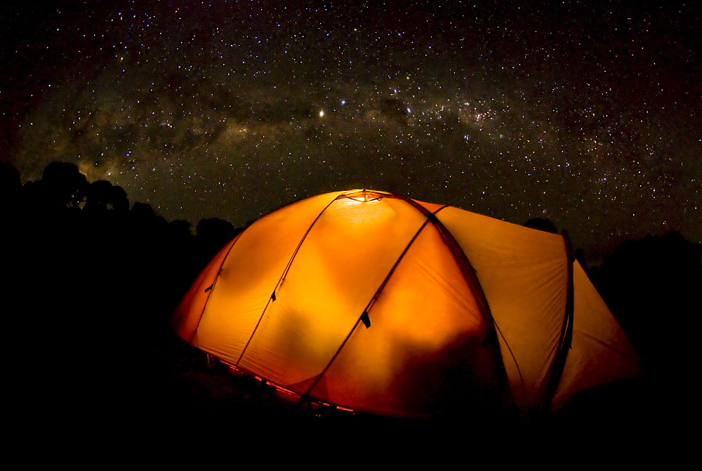 A tent illuminates the night as the Milky Way Galaxy floats above in a starry sky on Mt. Kilimnajaro.