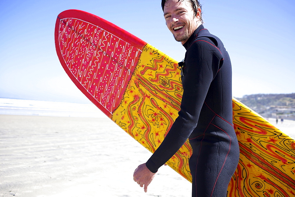 Male surfer runs towards the water while smiling.