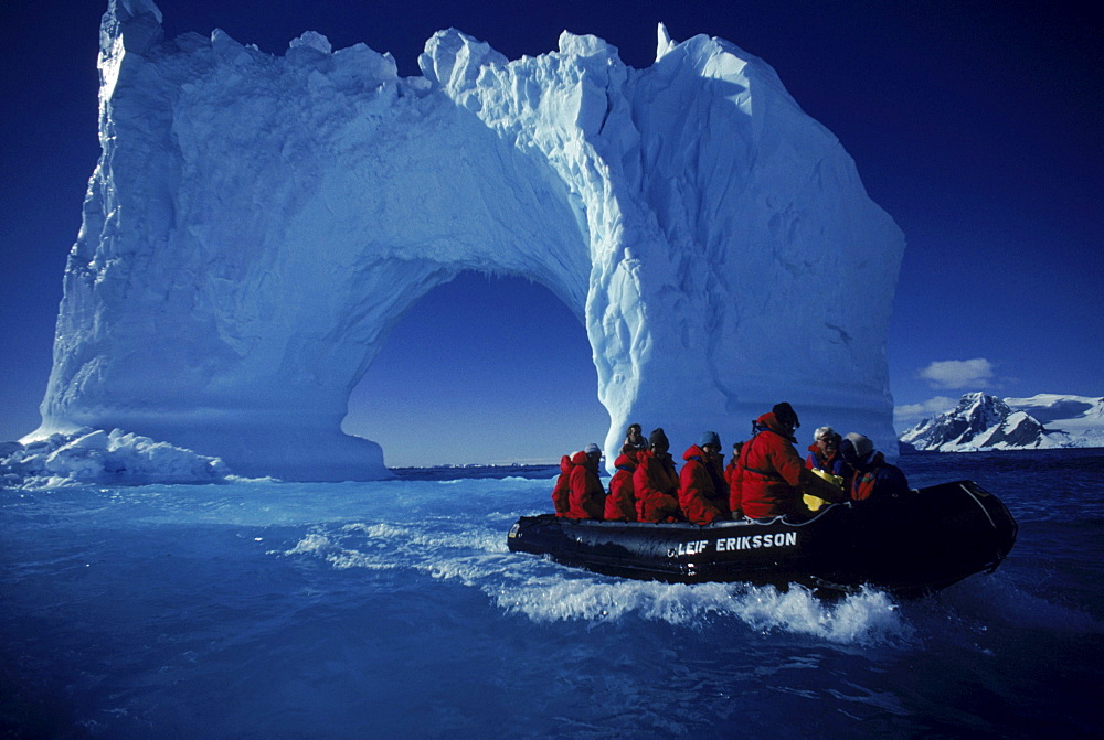 Boating by an iceberg arch near Yalour Islands, Antarctica.