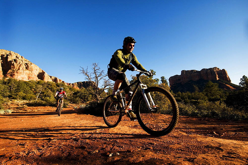 Two middle age men ride mountain bikes through the red rock country of Sedona, AZ.