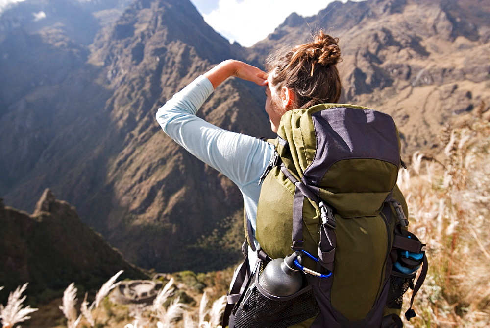 A young woman looks into the distance over some ancient Incan ruins along the Inca Trail.