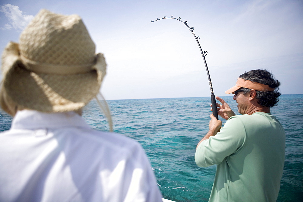 A fisherman reels in a fish as his pole bends down during the fight.