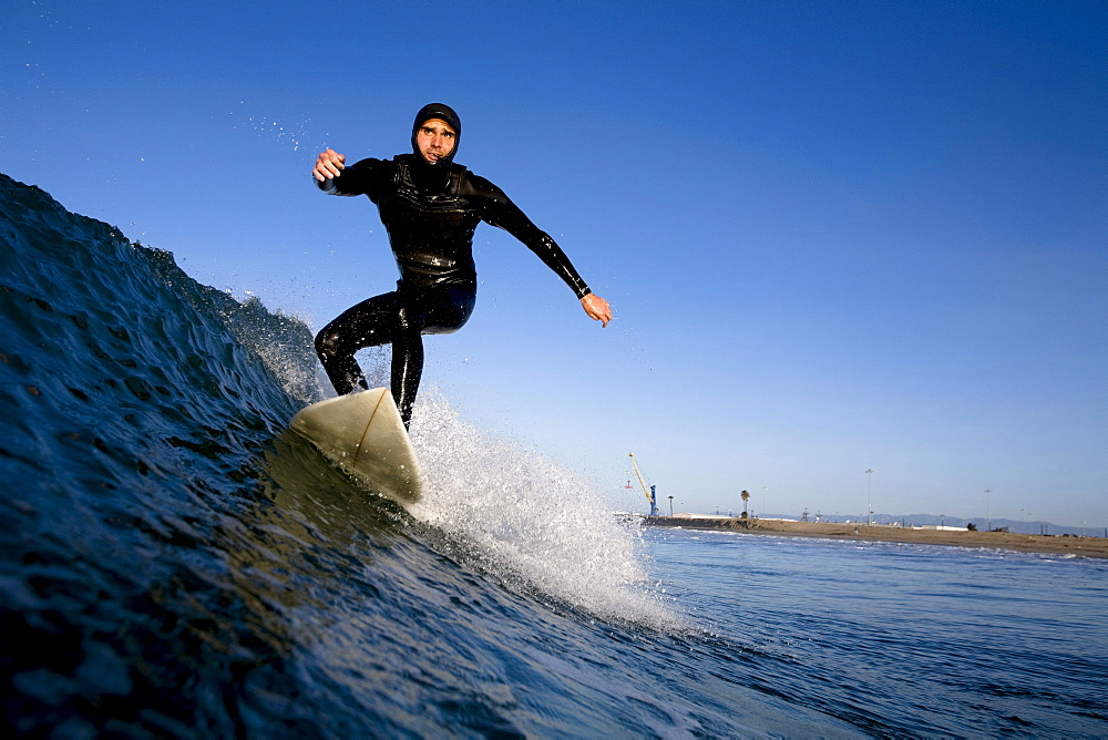 A surfer wearing a hood pumps down the line in Port Hueneme, California.