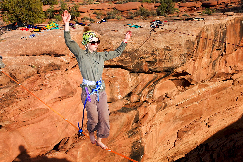 A female highliner walks across a highline at the Fruit Bowl in Moab, Utah, USA.