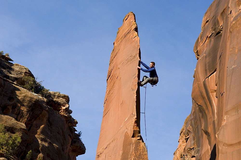 Man rock climbing up slender sandstone spire, Gateway, Colorado.