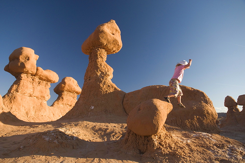 Young girl jumping off rocks in Goblin Valley State Park, Hanksville, Utah.