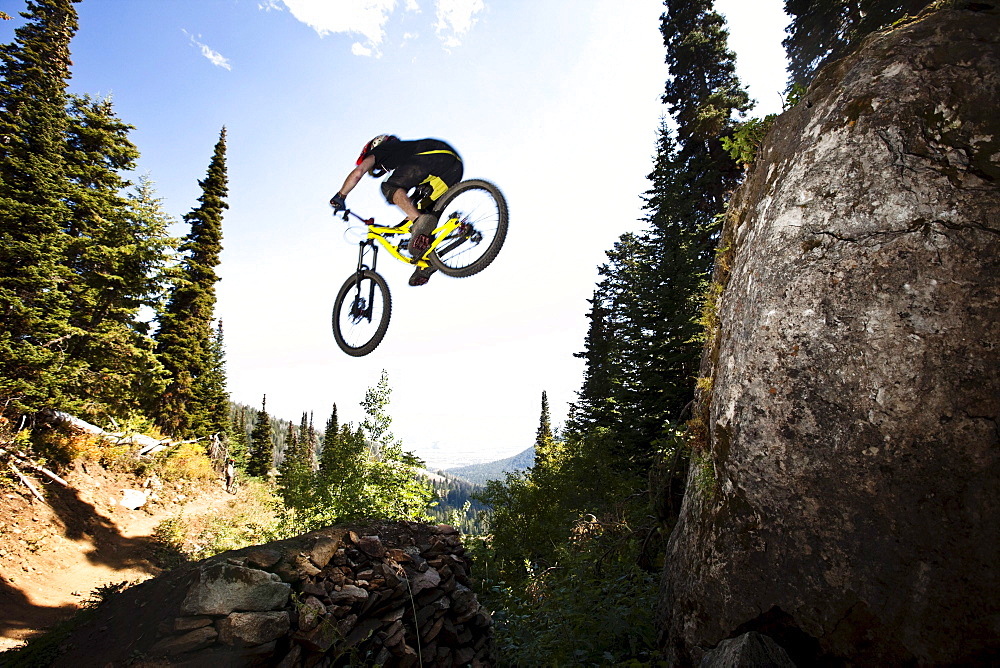 A athletic man mountain biking jumps off a large cliff while downhilling on Teton Pass in Jackson, Wyoming.