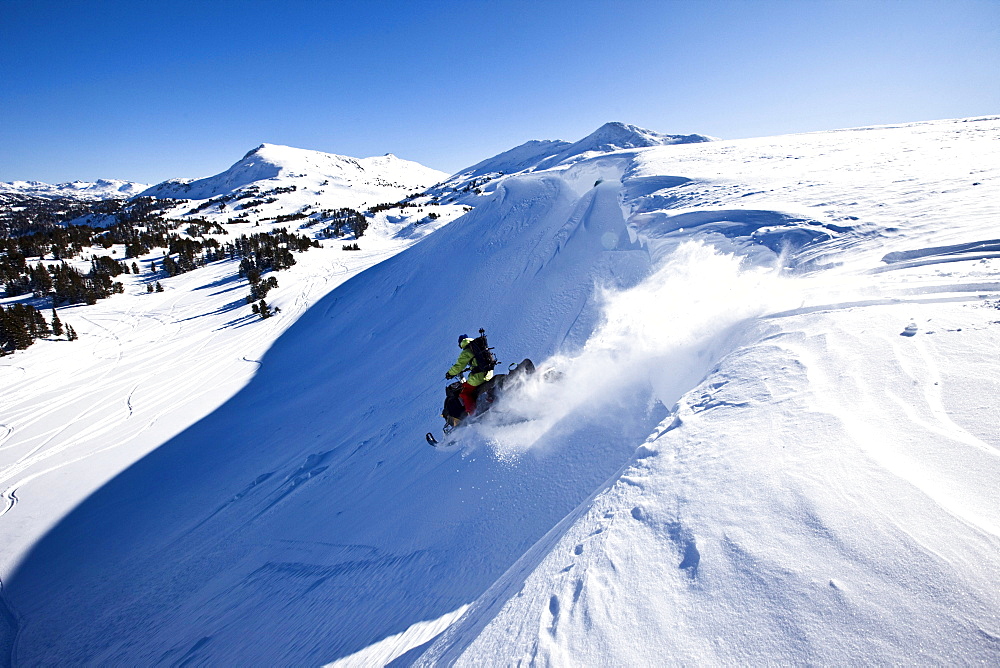 A snowmobiler jumping off a cornice on a sunny winter day in Cooke City, Montana.