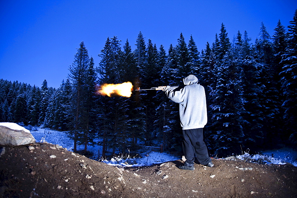 A young man shooting a large gun with a flame coming out of the barrel in Bozeman, Montana.