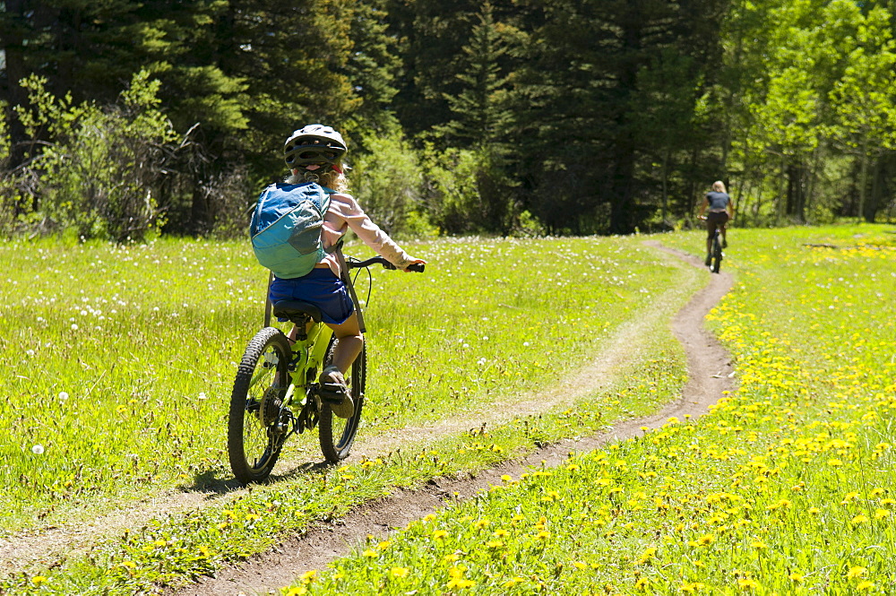 A young girl follows her mother while mountain biking the Valley Trail in Telluride, Colorado.