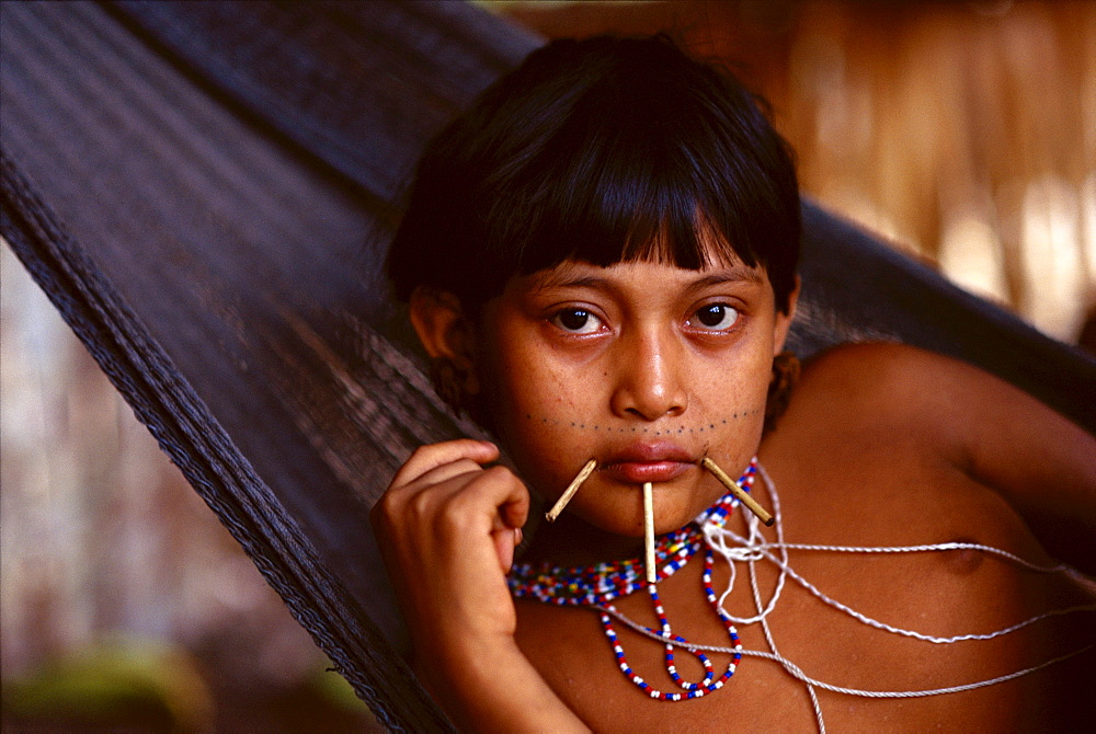 Yanomami Indian girl with sticks at the corners of her mouth and just below her lower lip and bead necklaces lies in a hammock in her village in the Amazonian Forest in southern Venezuela.