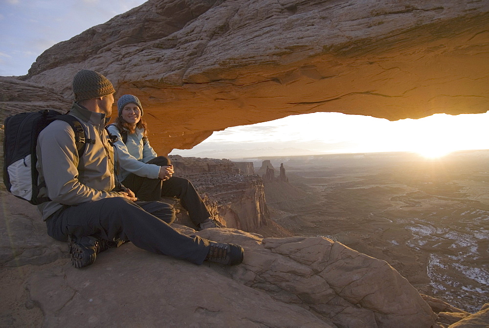 Man and woman hiking by rock arch.