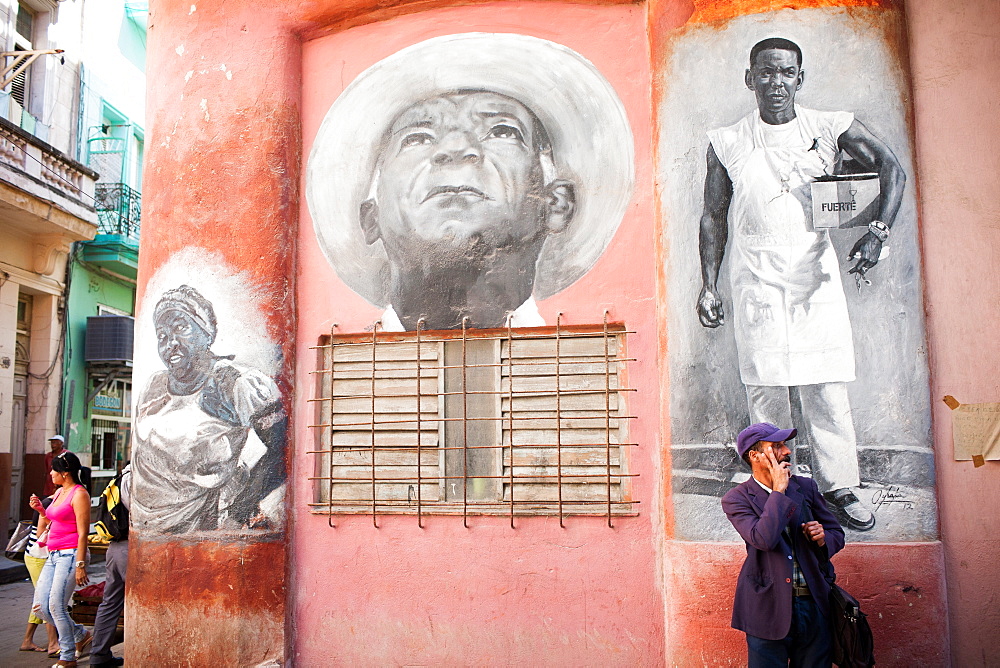 Pedestrians wait and walk by a mural painted on the side of a building in the old part of Havana, Cuba.