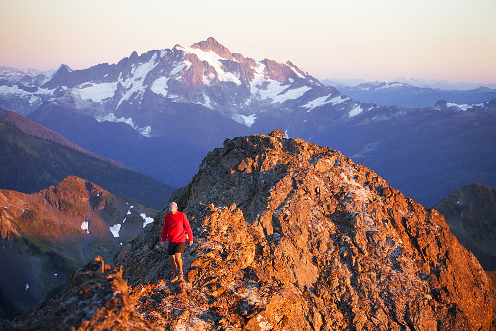 A hiker walks a rocky ridge with Mount Shuksan in the background, North Cascades National Park, Washington, United States